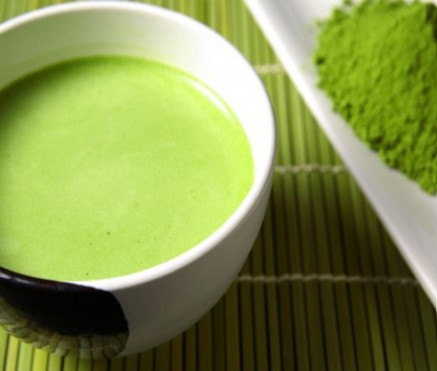 A small plastic measuring spoon on its side with a pile of vibrant spirulina powder against a white background